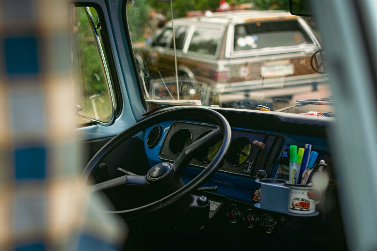 Home 1 Interior view of a vintage car featuring a classic dashboard, steering wheel, and outdoor view.
