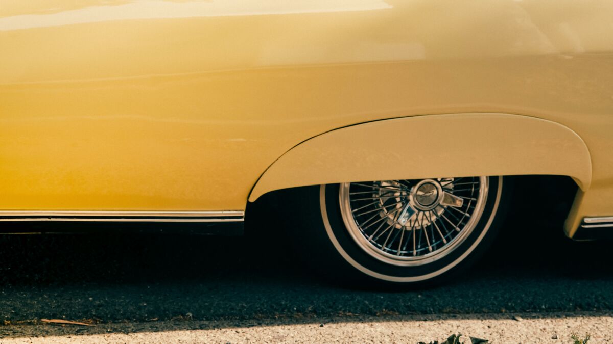 Home 5 Close-up of a classic yellow car featuring a shiny spoke wheel with a vintage aesthetic.